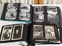 Two open vintage photo albums on a surface, showing pages with black-and-white photos of cats in the top album and family images from the 1920s in the bottom album.