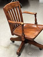 Side view of the wooden desk chair showing curved slatted back, armrests, and wheeled base.