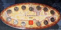 Top view of decorative matte box containing 1999 Canadian quarter set arranged over an oval map design. Each quarter is placed in designated circular slots. The box has noticeable wear on edges.