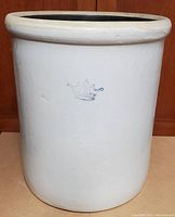 Front-facing photo of the antique ceramic crock showing the off-white glaze and blue crown mark on the exterior.
