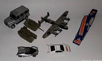 Seven diecast models including a silver Mercedes G Wagon, camouflage Lancaster bomber, two green tanks, a white Lotus Esprit 007 car, a silver illuminated car, and a blue Matchbox aircraft carrier.