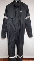 Front view of black one-piece Dry-Rider motorcycle rain suit with reflective strips on arms and lower legs, zipper front, elastic waist, and pocket flap.