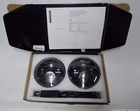 Photo showing two round LED headlights and a wiring harness secured in packaging foam inside a cardboard box.