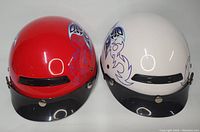 Two motorcycle helmets, red and white, viewed frontally showing the butterfly design on the sides and black detachable visors.