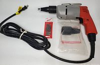 Full view of the Milwaukee drywall screw gun with long power cord, multiple screwdriver bits pack, and a sealed accessory.