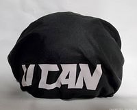 Photo of black drawstring helmet carrying bag with bold white 'U CAN' lettering across one side, showing the bag's corduroy texture.