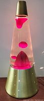 Full view of lava lamp showing pink wax formations in clear liquid inside conical glass, and aluminum base with small circular holes.