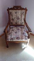 Front view of wooden armchair showing floral upholstery on seat and backrest and carved wooden frame