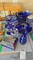 Overview of the blue glass bowls, pitcher, vases, and music box arranged on a table.