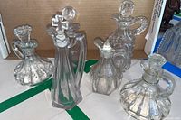 Photo showing all six clear glass oil bottles with distinct stoppers and shapes on a white surface with a cardboard background.