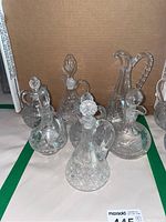 Seven glass cruets arranged together showing various shapes, sizes, and stopper designs with etched and faceted patterns.