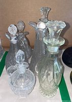 Four variously shaped glass cruet bottles with stoppers, placed on a flat surface with a cardboard background