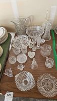 Full view of crystal and glass items including plates, pitchers, bowls, and small dishes on wooden table