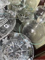 Photo showing clear etched glass bowls and candy dishes with floral and grapevine patterns, including pieces with starburst bases and scalloped edges.