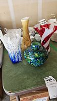 Four hand blown glass vases displayed together on a green table.