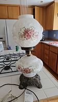 Full view of the vintage hurricane lamp showing white floral embossed glass and painted pink flowers with metal base.