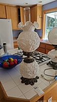 Full view of vintage milk glass table lamp with two embossed floral globes and clear glass chimney on ornate brass base.