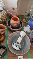 View of several pottery bowls and vases on a wooden surface, showing varied shapes and decorated with earth tone and black geometric patterns.