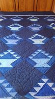 Full view of one blue patchwork quilt showing basket and geometric designs in various blue shades with floral quilting stitching.