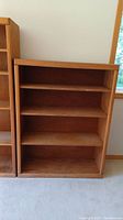 Front view of one wooden bookshelf showing four shelves with natural wood grain and wear marks.