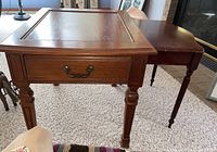 First wooden table with drawer, carved legs and brass handle, medium wood tone.