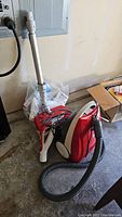 Kenmore red canister vacuum with hose and wand, showing vacuum body and hose coiled on the ground.