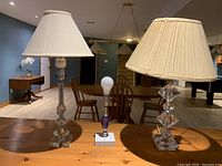 Three glass lamps on a wooden table, two with lampshades, one without. Decorative glass bases, one with purple accents.