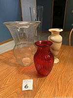 All four vases displayed on a wooden table: red ribbed glass, two clear glass, and alabaster vase at the back