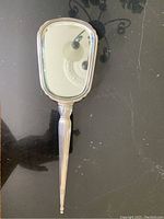 Front view of antique sterling silver hand mirror showing reflective glass and silver frame.