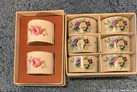 Photo showing set of 2 Coalport Shrewsbury china napkin rings with pink roses and blue flowers, placed in original box with orange insert.