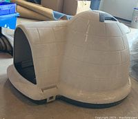 Side view of beige plastic resin igloo-shaped dog house with visible wear