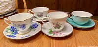 Four fine bone china tea cups and saucers displayed on wooden table, showing cup and saucer top and side floral designs.