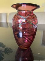 Front angled photo of burgundy glass vase showing silver swirl patterns and glossy finish on reflective table surface.