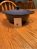 Front view of Le Creuset cobalt blue pot with lid and side handles on wooden table alongside a lot number card.