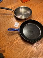 Top view of Kenmore stainless steel frying pan with polished interior and Le Creuset blue cast iron frying pan, showing cooking surfaces and handles.