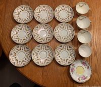 Top view of 9 Royal Albert 2443 saucers, 3 matching teacups, 1 Reverie series saucer, and 1 Misty Rose teacup without handle on wood table