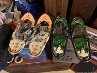 Two pairs of youth snowshoes on a surface: Tubbs Trail Adventure 21 (cream and orange) and GV Canadian Trail Junior 21 (green and black).