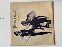 Front cover of Fleetwood Mac Rumours album with artistic pose of two band members on beige background.