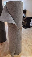 Large standing roll of grey acoustic cloth fabric with some edges folded back.