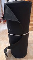 Full view of large roll of black acoustic cloth standing on floor showing fabric texture and roll size