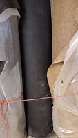 Photo of black acoustic cloth roll wrapped with orange string, showing the front side of the roll.