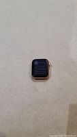 Apple Watch SE powered on screen showing battery icon with red charging bolt on a beige surface.