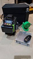 Laser level device, remote control, green adjustable mount, metal mounting plate, and black carrying case displayed on a table.