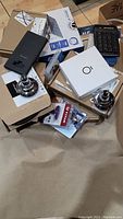Photo showing various items including black electronic keypad lock, two chrome door knobs, Yale door lock set packaging, and other boxes on floor.