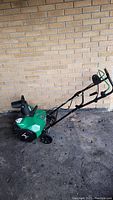 Full side-angle view of green electric snow blower with black and green handle grips and wheels.