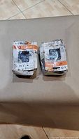 Two original Stihl chainsaw chains in their packaging on a cloth surface, boxes worn but intact.