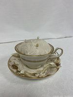 Wedgwood bone china cup on saucer with fabric pin cushion and decorative pins inserted, gold Florentine pattern.