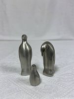 Three pewter penguin figurines on white fabric background, showing front and side views.