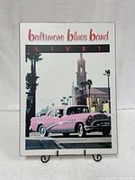 Front view of wooden poster showing the Baltimore Blues Band live text with vintage car and building image.