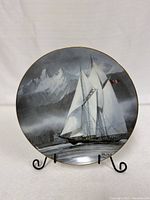 Front of the collector's plate showing the image of the Bluenose schooner sailing in front of mountain scenery with Canadian flag, displayed on stand.
